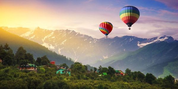 Two colorful hot air balloons float over a lush green valley with mountains at sunset.
