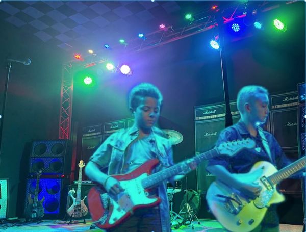 Two young musicians playing electric guitars on a stage with colorful lights.