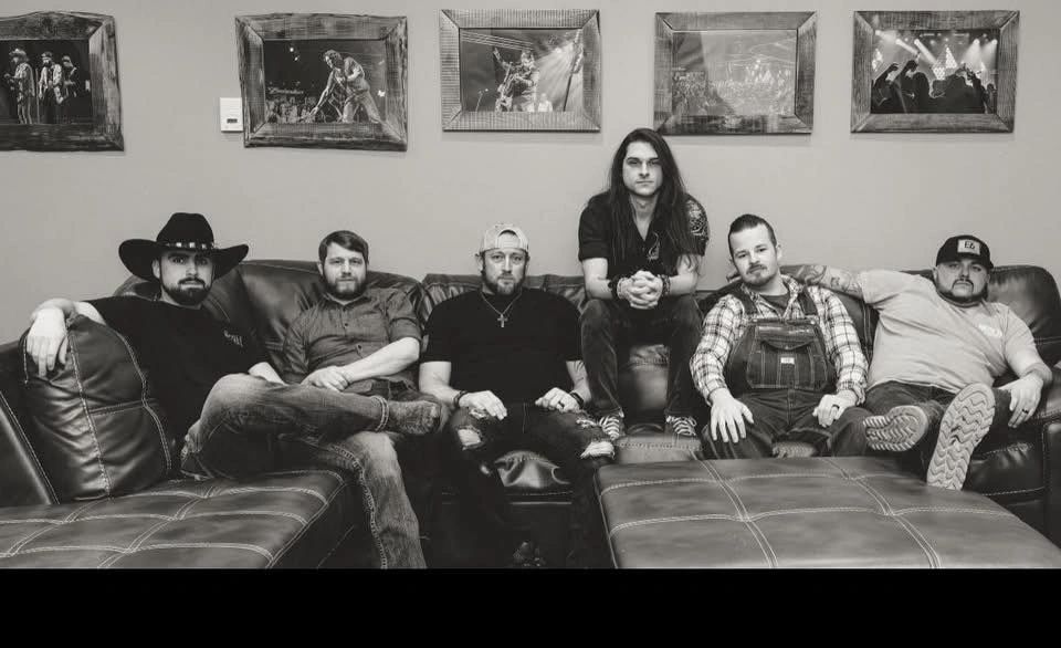 Six men sitting on a leather couch in a black and white photo.