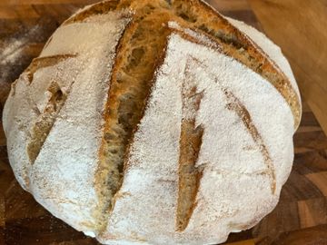 A freshly baked round loaf of artisan bread with a dusting of flour.