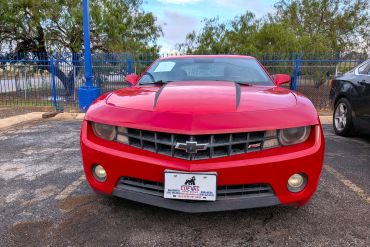 Red Chevrolet Camaro parked outdoors with black racing stripes.