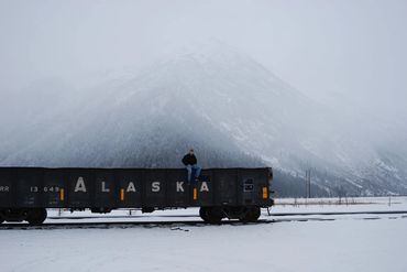 Man sitting atop a train car in a snowy landscape with a mountain in the background