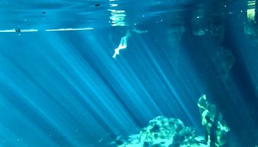 Underwater image of a woman swimming in a deep blue spring with sunlight rays penetrating the water