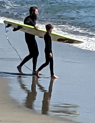 A man and a boy walking toward the ocean with a surfboard