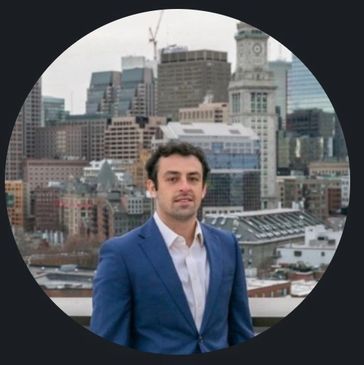 Man in blue suit standing on rooftop with cityscape background.
