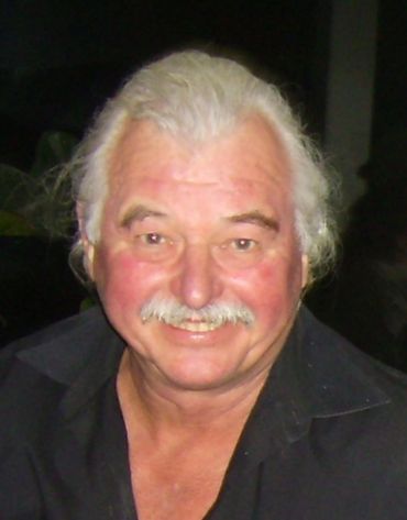 Smiling elderly man with white hair and mustache in black shirt.