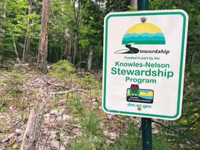 Sign for Knowles-Nelson Stewardship Program in a wooded area.