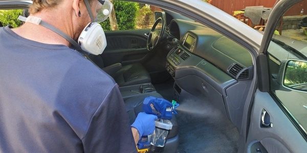 Person wearing protective gear disinfecting a car's interior.