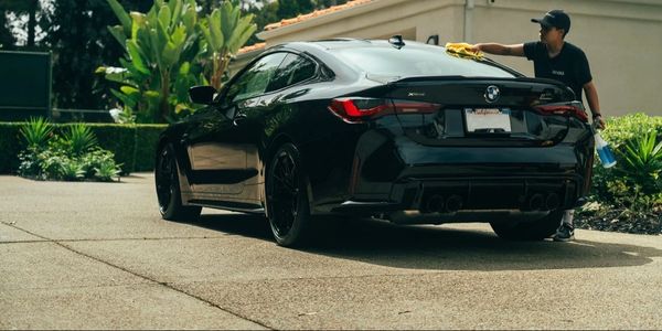 Person detailing a sleek black BMW car in a sunny driveway.