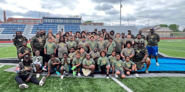 Large group of kids and adults posing on a football field.