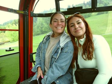 Two women smiling inside a cable car with green hills outside.