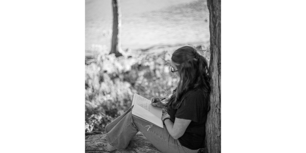 A woman sitting by the creek writing in her journal. Journaling is important for healing.