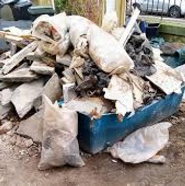 A pile of construction debris and garbage in a blue container outdoors.