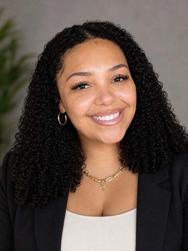 Smiling woman with curly hair and gold jewelry.