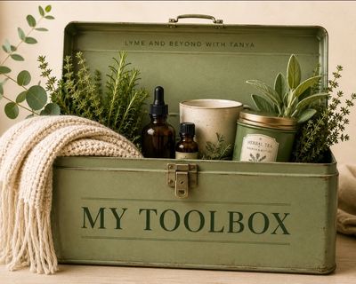 A green toolbox labeled 'MY TOOLBOX' filled with herbs, essential oils, and a knitted cloth.