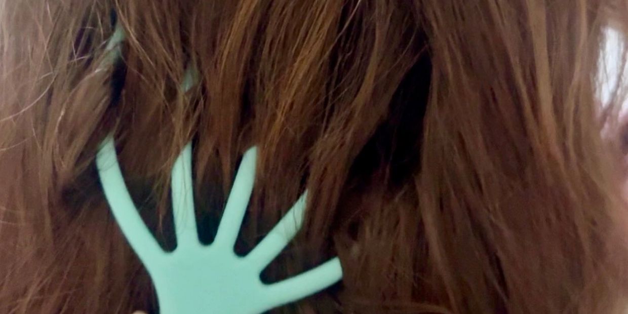 A unique teal hair comb shaped like a hand in brown hair.