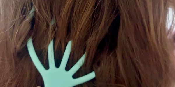 A unique teal hair comb shaped like a hand in brown hair.
