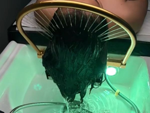 Person washing hair under a unique curved showerhead with water flowing down.