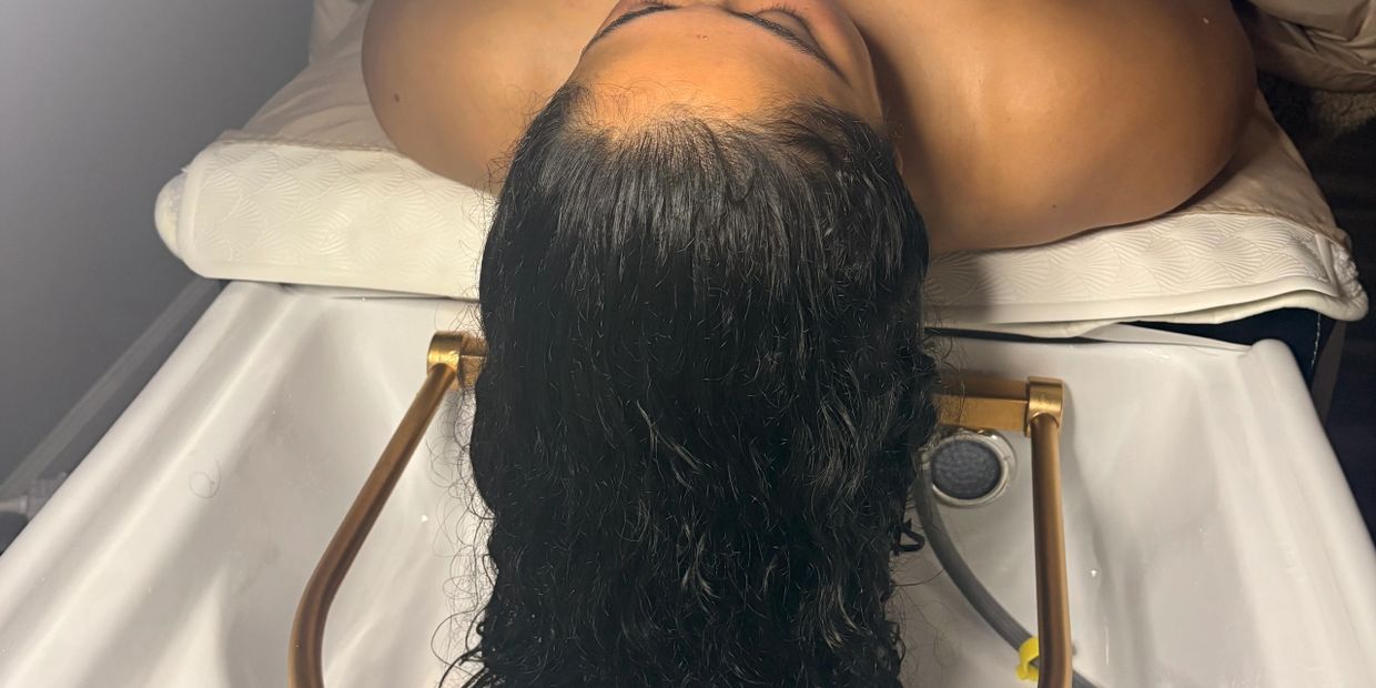Person with wet hair lying back on a salon wash basin.