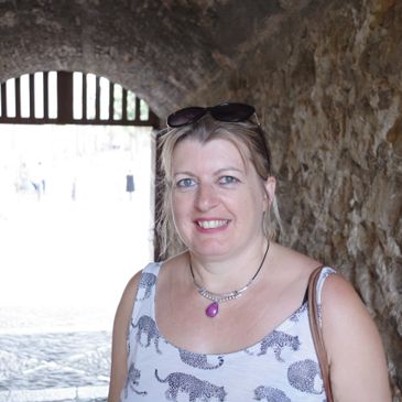 Smiling woman standing in a stone archway with sunglasses on her head.