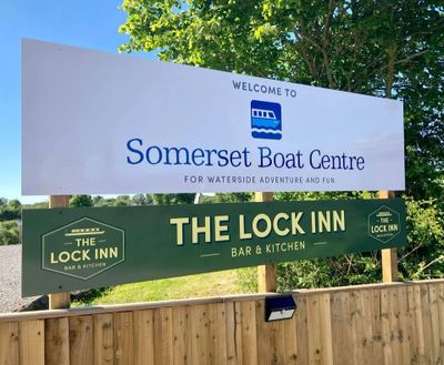 Welcome signs for Somerset Boat Centre and The Lock Inn bar and kitchen outdoors.