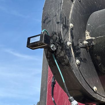 Close-up of a black device attached to a large industrial fan outdoors under a blue sky.