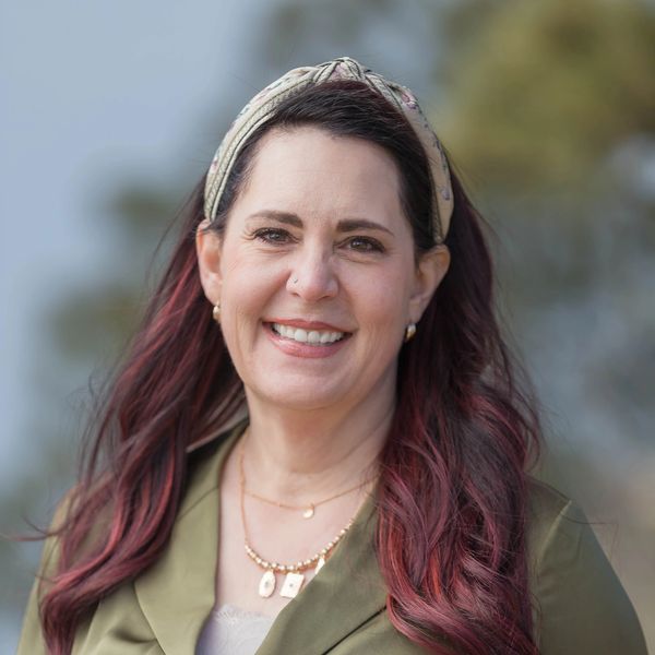 Smiling woman with long wavy hair and headband outdoors.