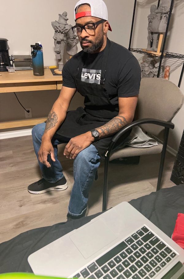 Man with tattoos and glasses sitting in a chair wearing a Levi's shirt and apron.