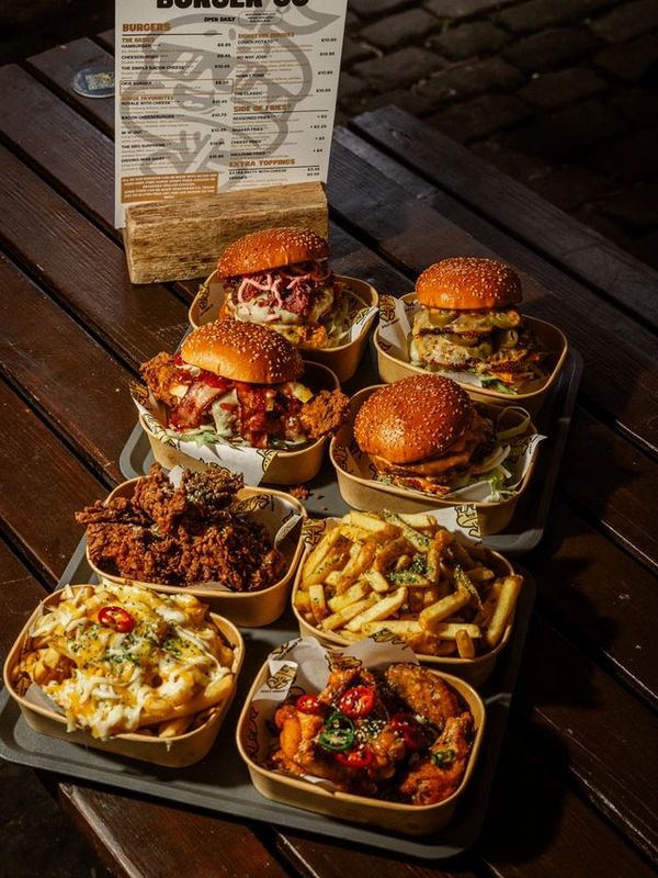 Tray with burgers, fried chicken, loaded fries, and wings on a wooden table.