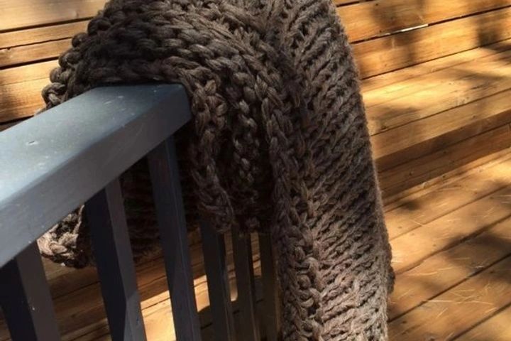 Chunky knit brown scarf draped over a blue railing.