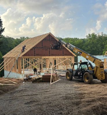 Construction workers building a wooden house frame with a forklift nearby.