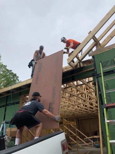 Three men lifting a large panel during house construction.