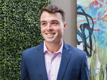 Smiling man in blue blazer and pink shirt.