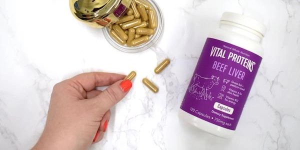 Hand holding a capsule near a bottle of Vital Proteins Beef Liver supplements.