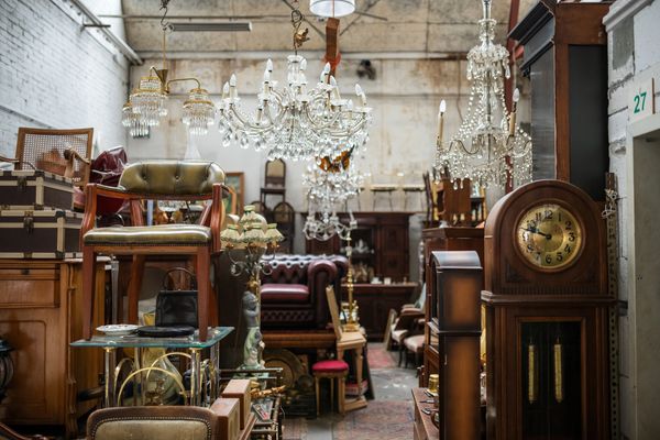 A cluttered antique shop filled with furniture, chandeliers, and a grandfather clock.