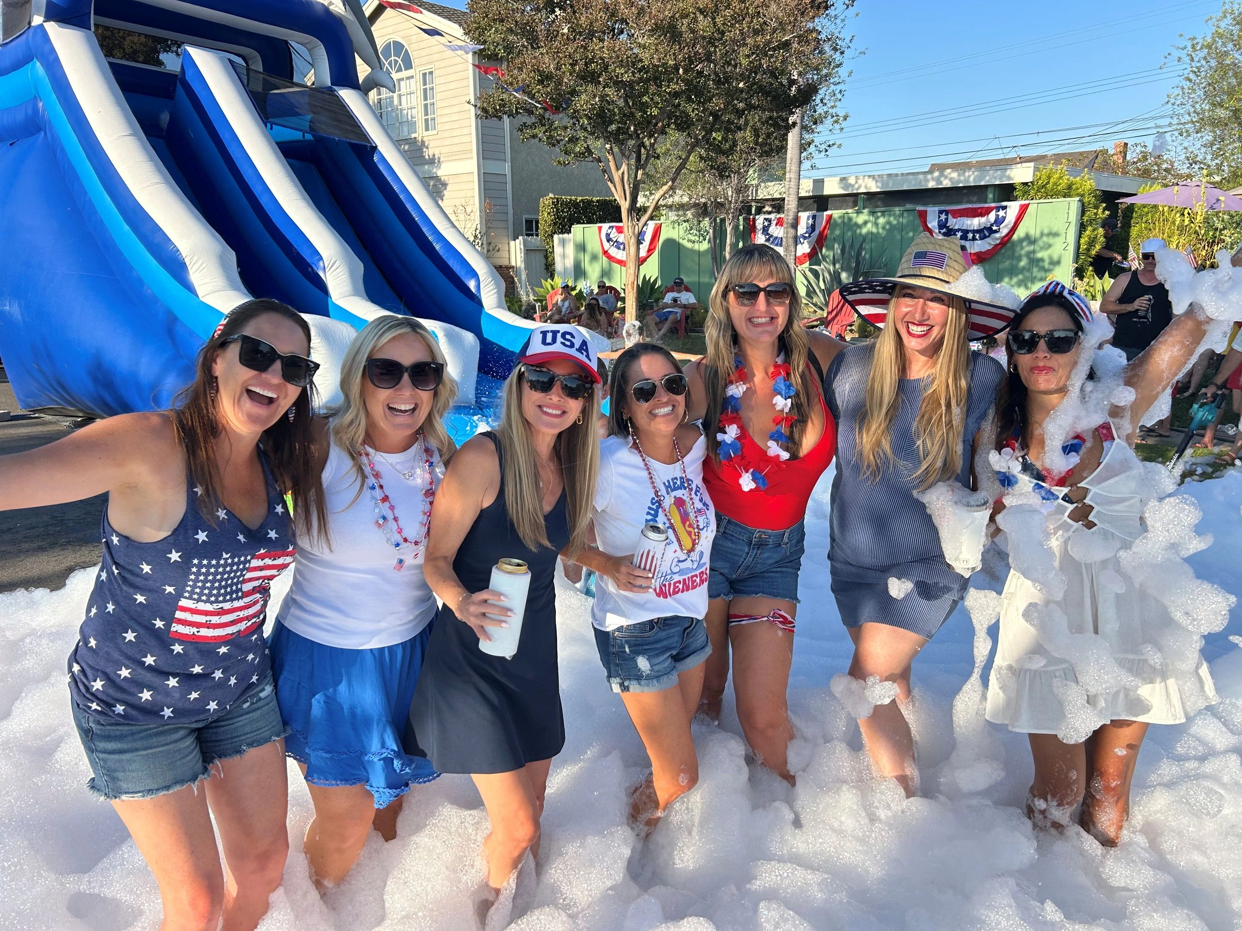 Group of women enjoying a foam party with patriotic USA-themed attire and decorations.