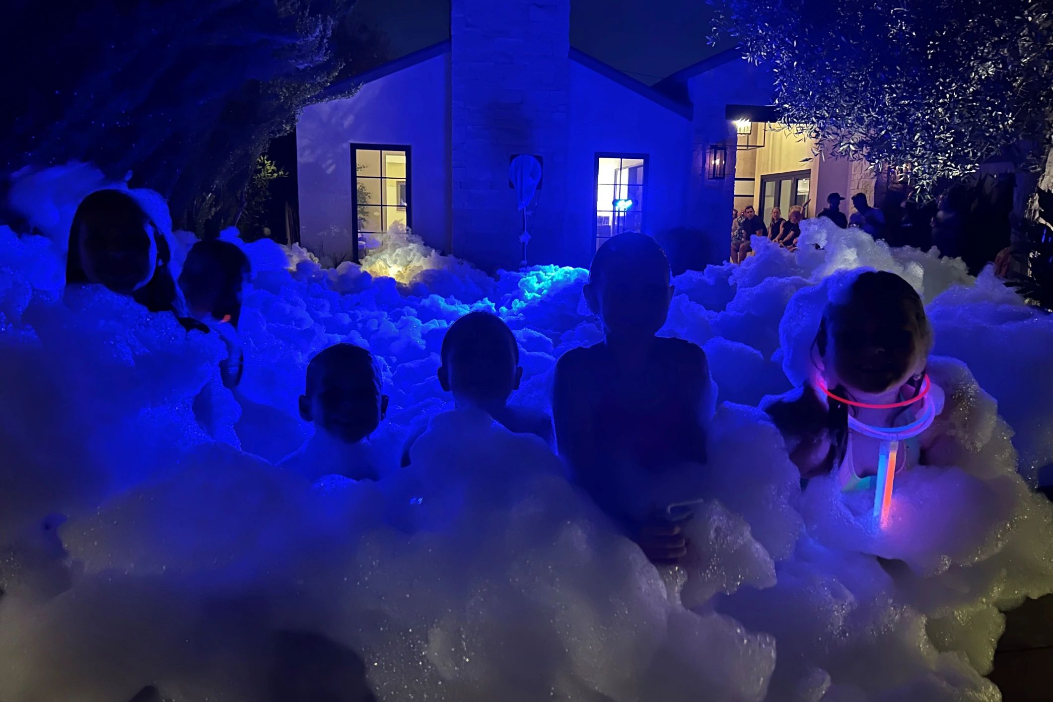 Children playing in glowing foam at a nighttime party outside a house.