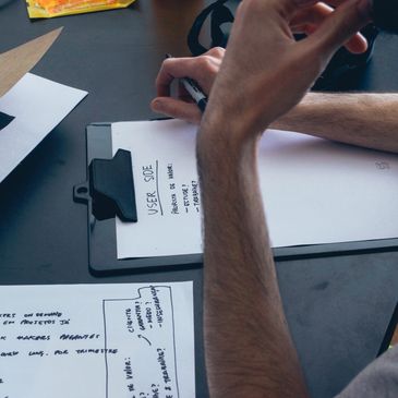 Person writing notes on a clipboard at a desk with papers scattered around.