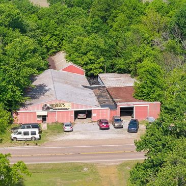 A rustic building labeled Frisbee's with several parked cars surrounded by dense green trees.