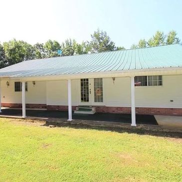 White house with a green metal roof and a covered porch.