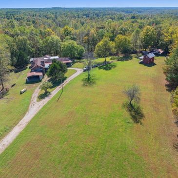 A rural property with houses surrounded by trees and open grassy land.