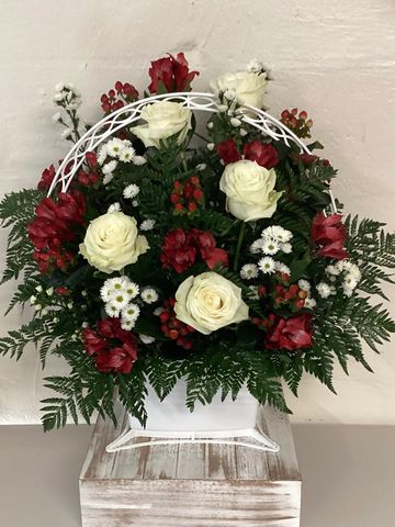 White roses, red alstroemerias, red hypericum, and white aster presented in a basket.