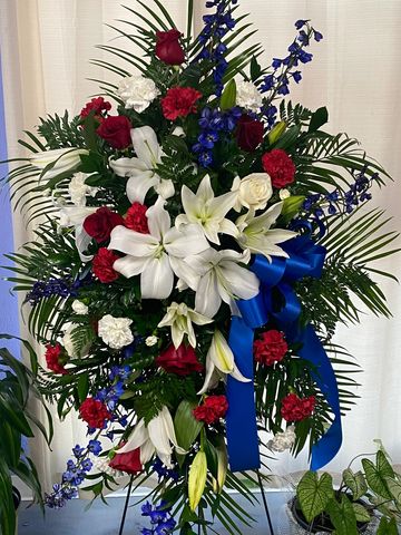 Blue Delphinium, White Lilies, Red Roses, and carnations present a stunning patriotic tribute. 