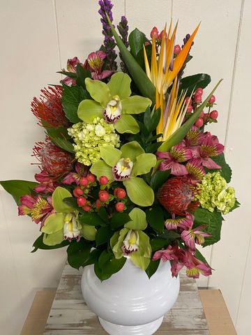 Colorful floral arrangement in a white vase with orchids and tropical flowers.