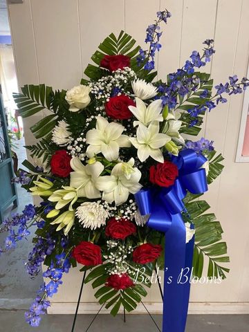 Blue Delphinium, White Lilies, Red Roses, and white mums present a stunning patriotic tribute. 