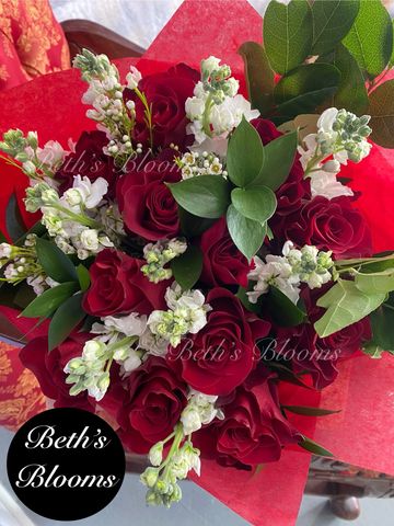 A vibrant bouquet of red roses and white flowers with green leaves wrapped in red paper.