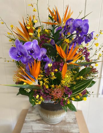 Vibrant tropical flower arrangement with purple orchids and orange bird of paradise.