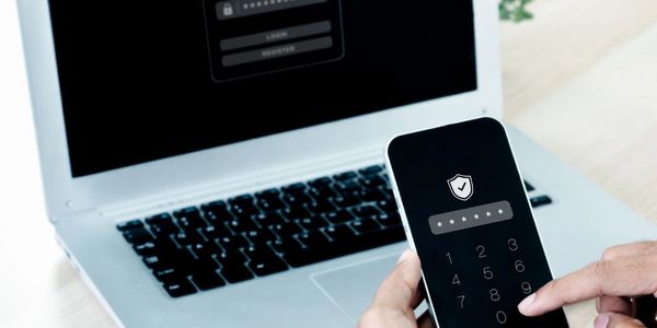 Person entering a security PIN on a smartphone for two-factor authentication with a laptop login screen in the background.