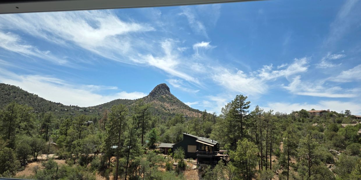 A scenic mountain view with a cabin amidst tall trees under a blue sky.