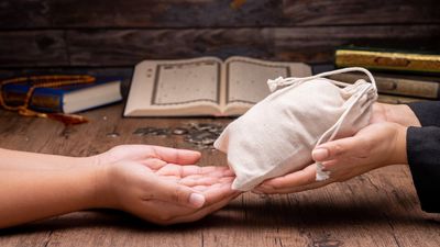 One person handing a white pouch to another on a wooden table with books in the background.
